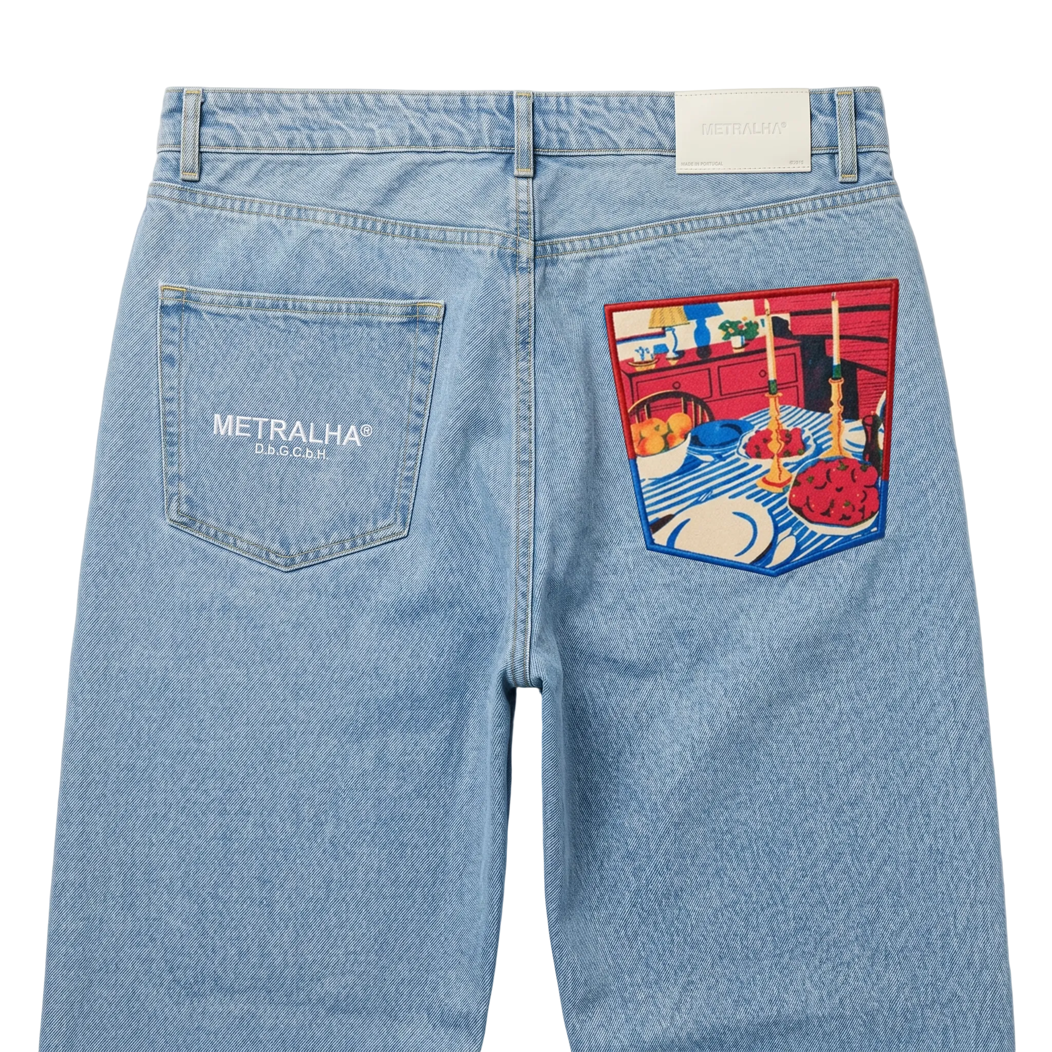 Light blue denim jeans shown from the back, featuring a white METRALHA logo on the right back pocket and a large colorful patchwork graphic on the left back pocket.