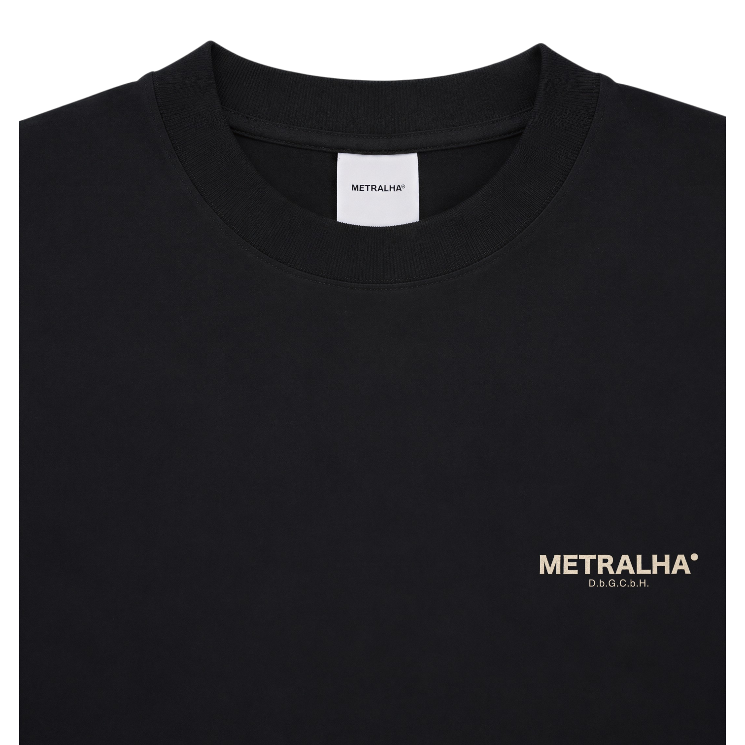 A close-up of a black crewneck t-shirt with a small gold METRALHA logo printed on the left chest. The white neck label also displays the brand name 'METRALHA'.