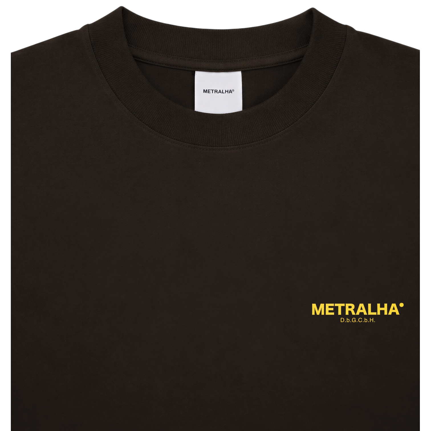 A close-up of a brown chocolate crewneck t-shirt featuring the brand name 'METRALHA' printed in yellow on the left chest, with a white brand label visible inside the collar.