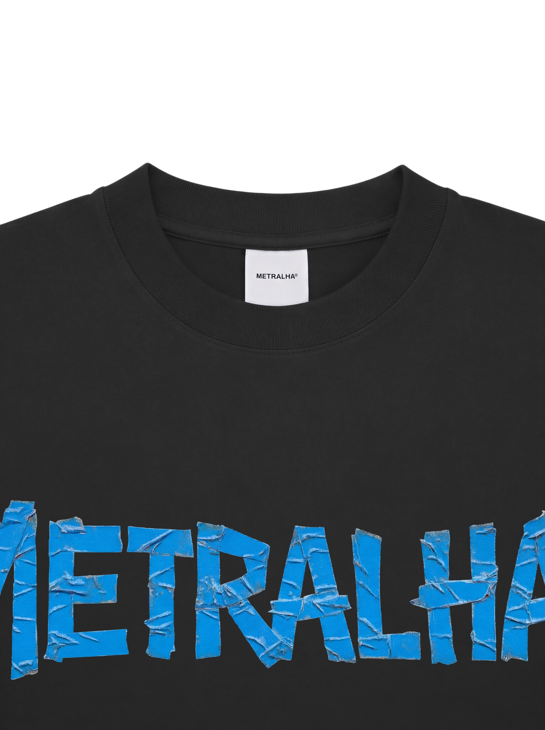 Close-up of a black crewneck t-shirt featuring a large blue 'METRALIA' graphic across the chest with a textured, torn-paper effect. The inner neck label shows the brand 'METRALIA'.